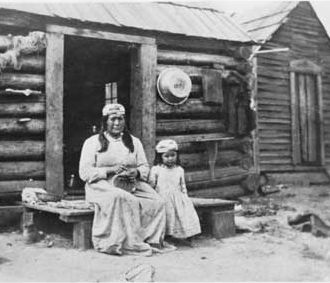 Native American woman and child in front of log cabin