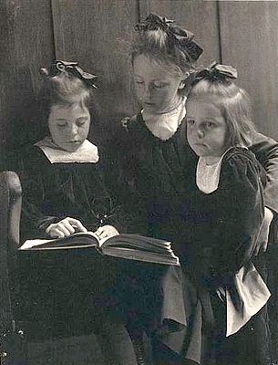 Three young girls reading a book.